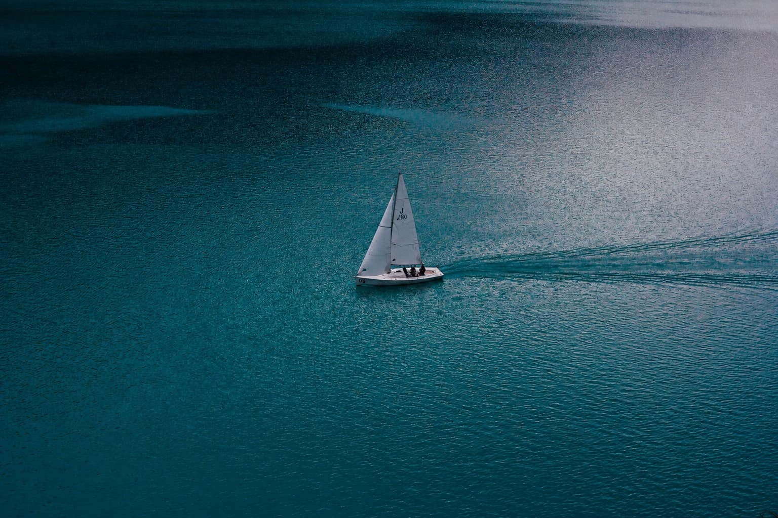 A lone J/80 sailing across calm teal water